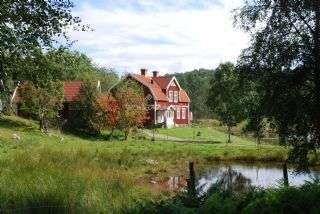 L'image représente une scène rurale sereine avec une grande maison au toit rouge, située au bord d'un étang tranquille et entourée d'une végétation luxuriante.