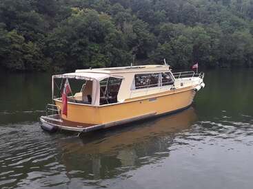The image depicts a yellow boat with a white canopy on a river, featuring a red flag attached to the back and a Canadian flag flying from the front.