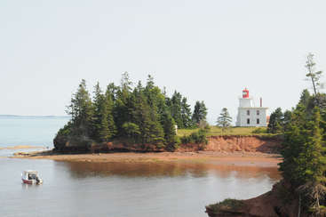 The image depicts a serene coastal scene, featuring a tranquil body of water, a small island, and a prominent structure resembling a lighthouse or pier, surrounded by lush greenery.