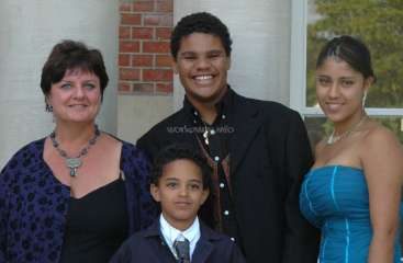 The image depicts a family of four posing for a photo, with a woman, a man, a young boy, and a girl, all dressed in formal attire.