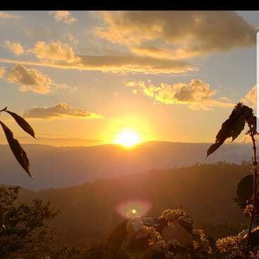 The image depicts a breathtaking sunset over a mountain range, with vibrant yellow and orange hues illuminating the sky and clouds.