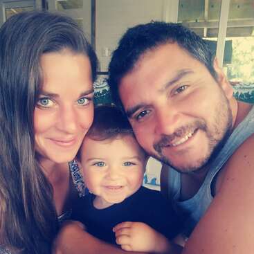 The image depicts a family of three posing for a selfie, with the woman on the left, the baby in the middle, and the man on the right, all smiling.