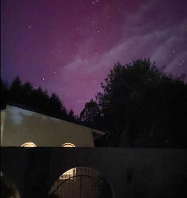 The image depicts a serene nighttime scene featuring a building with arched windows, trees, and a vibrant purple sky dotted with stars.