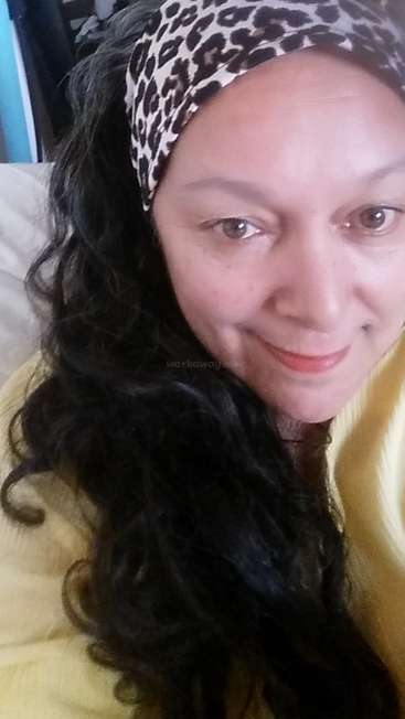 The image shows a woman with long dark hair wearing a leopard print headband and a yellow sweater, posing for a selfie.