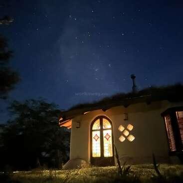 The image depicts a house with a stained glass window at night, set against a starry sky. The house is illuminated from within.