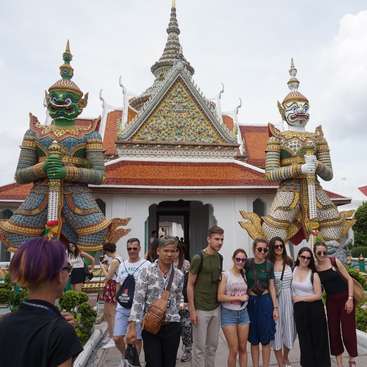 The image depicts a group of people standing in front of a temple, with two large statues of mythical creatures flanking the entrance. The temple\'s roof is adorned with intricate designs.